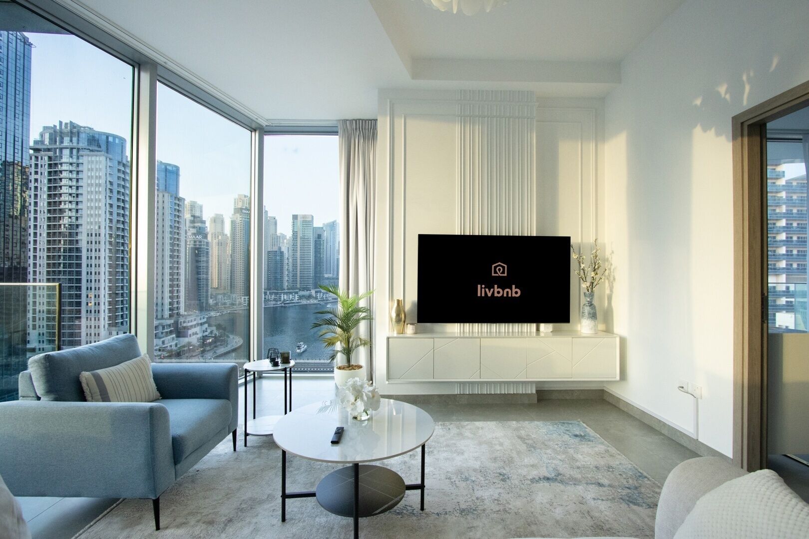Uma sala de estar moderna com uma janela grande, uma TV de tela plana, um sofá, uma mesa de centro e uma planta em vaso.