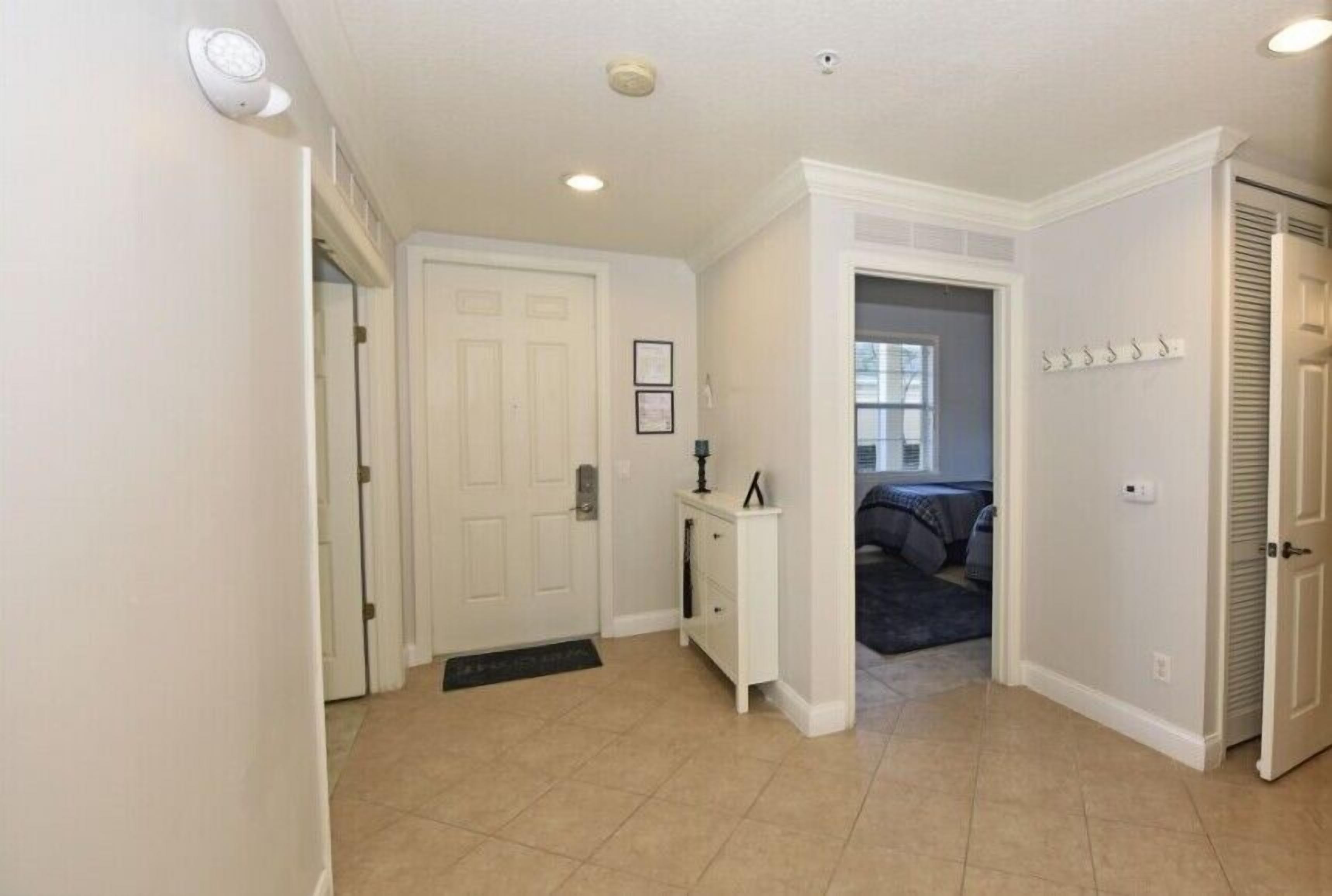 A hallway with a white door, a small white console table with a lamp, and a door with a coat rack.