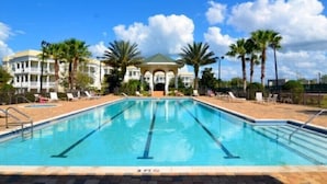 A swimming pool with lounge chairs and palm trees, surrounded by buildings with a covered area in the center.