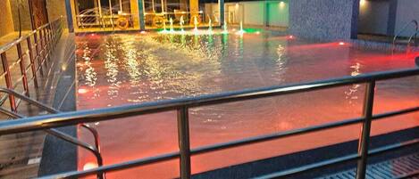 A swimming pool area with a covered seating area and a water fountain.
