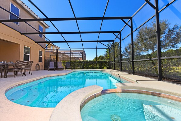 A swimming pool with a curved design, surrounded by a covered patio area with chairs and a table.