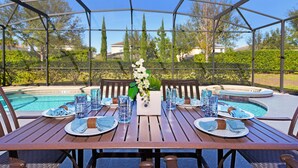Un área de comedor al aire libre con piscina, cubierta por un techo transparente y rodeada de follaje.