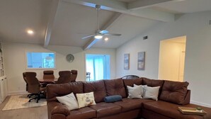 Ein geräumiges Wohnzimmer mit einem braunen Ledersofa, einem Essbereich mit Tisch und Stühlen sowie einem Deckenventilator.