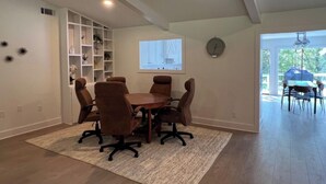 Ein geräumiger Raum mit einem Holzespeisetisch und vier Stühlen, einer eingebauten Bücherwand, einer Projektionsleinwand und einer Wanduhr.