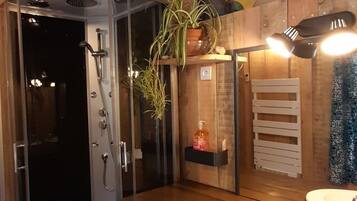 Une salle de bain compacte dotée d’une douche à parois de verre, d’un lave-linge encastré, d’un meuble-lavabo en bois et d’une fresque colorée sur le mur.