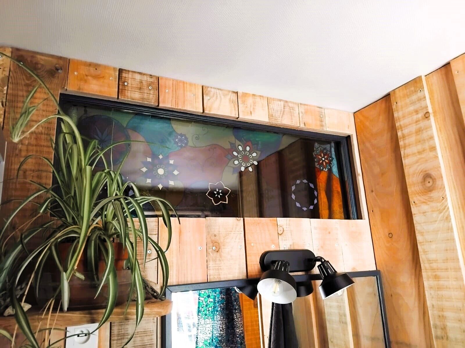 Une pièce aux murs recouverts de lambris en bois, avec une plante en pot et une œuvre d’art encadrée.
