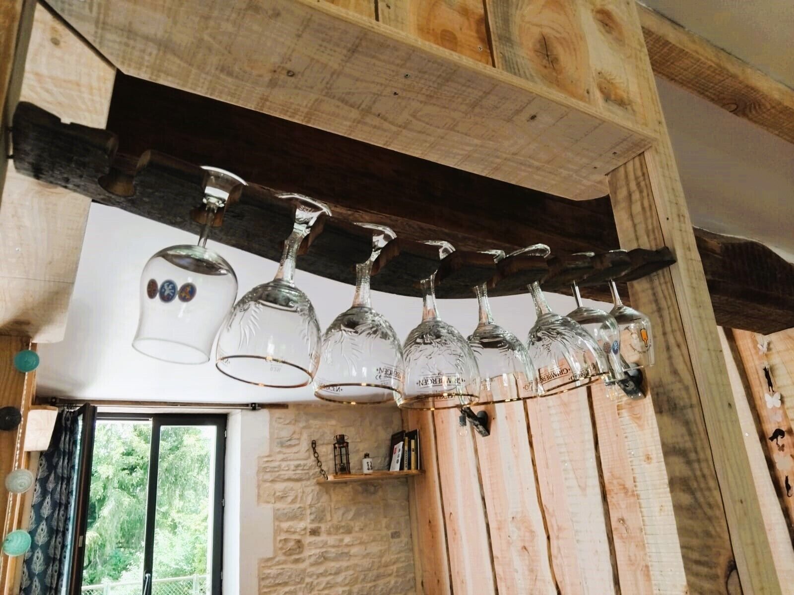 Un interior rústico con vigas de madera, una pared de piedra y una estantería con libros y un farol.