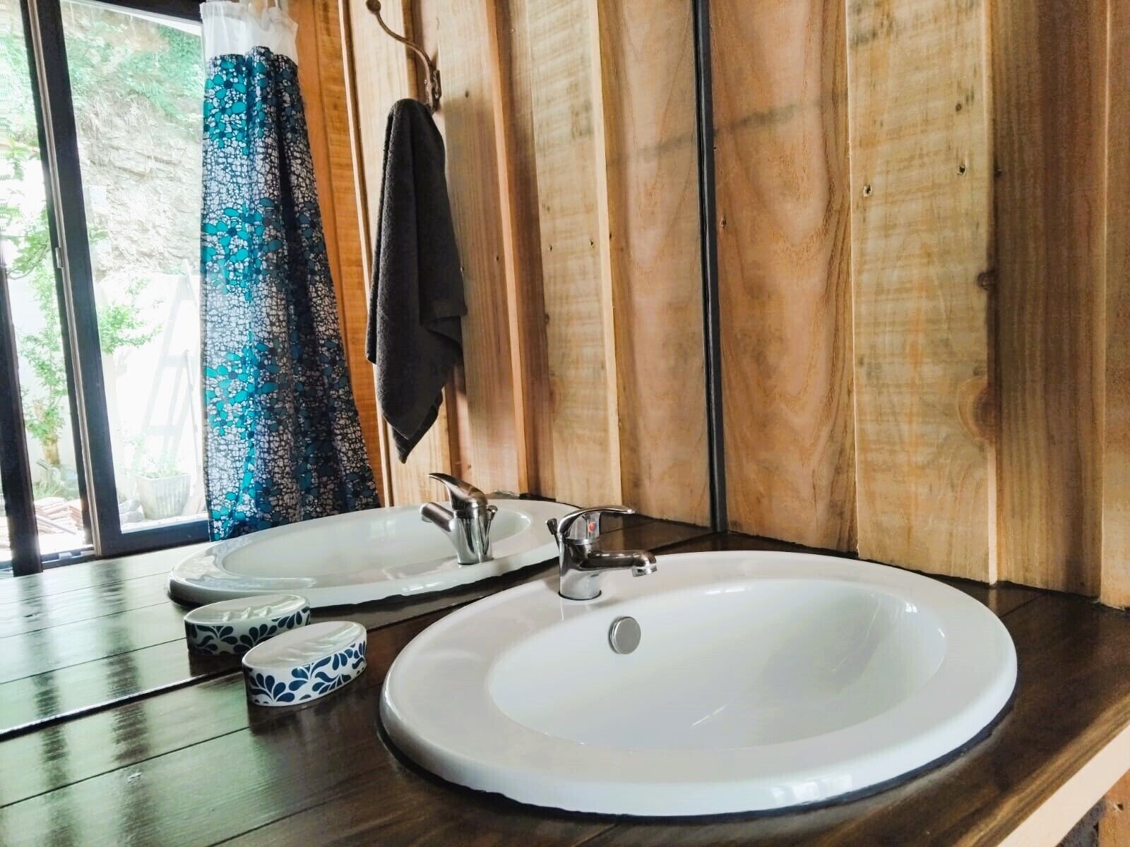 Une salle de bain avec un meuble-lavabo en bois, deux vasques et une fenêtre donnant sur un paysage verdoyant.