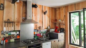 Una cocina con paredes de madera, estufa a gas, campana extractora y ventana con vistas a la vegetación.