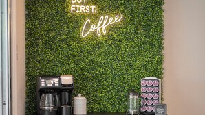 Un coin café en bois foncé, avec un mur vert en arrière-plan et un panneau néon sur lequel on peut lire : « D’abord, un café ».