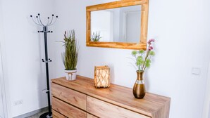 Un aparador de madera con un espejo encima, una planta en maceta, un farol y un jarrón con flores.