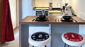 A modern kitchen with a microwave, stove, and stools labeled "Chamoises 2 Piste" and "Les Flocons 1 Piste".