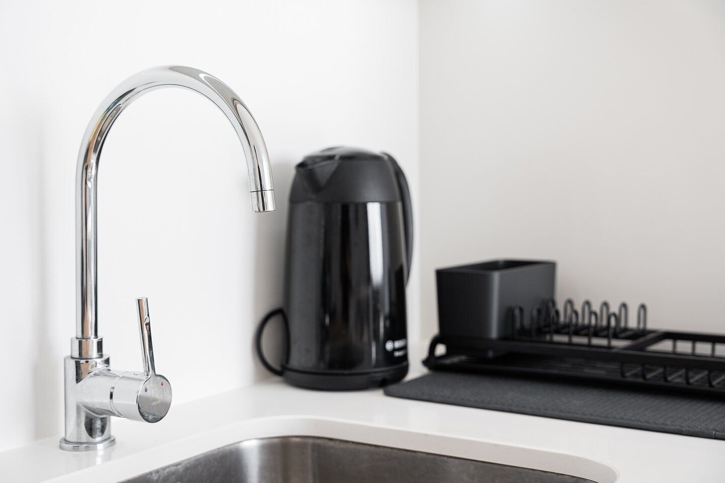 A modern kitchen with a stainless steel sink, a black coffee maker, and a black tray with utensils.