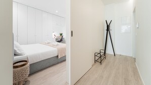 A modern bedroom with a bed, bedside table, and a desk with a chair. There is a black tripod on the floor and a small basket on the bed. - GuestReady - Urban chic in Aveiro (Aveiro)