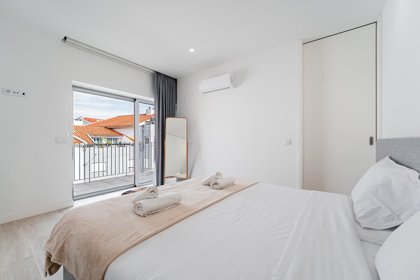 Une chambre d’hôtel moderne dotée d’un grand lit, d’une porte-fenêtre coulissante donnant sur le balcon, d’un système de climatisation intégré et offrant une vue sur le paysage urbain.