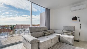 A modern living room with a sectional sofa, a floor lamp, and a view of the cityscape through large windows. - GuestReady - Urban chic in Aveiro (Aveiro)