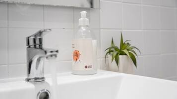 A bathroom sink with a clear glass bottle of hand soap labeled "Guest Ready" and a potted plant.