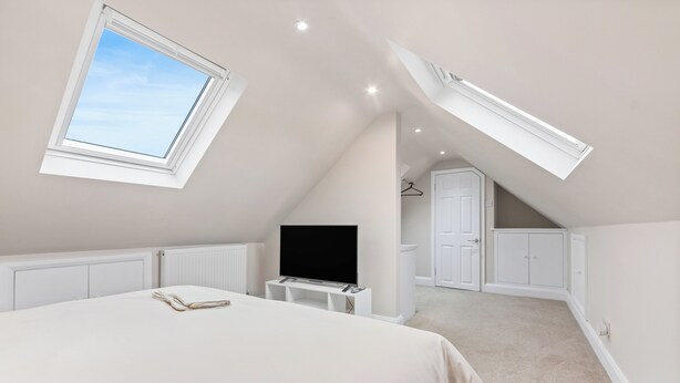 A bedroom with a sloped ceiling, a skylight, a bed, a TV, and a walk-in closet. - Modern Serenity in Langley Vale (Epsom)