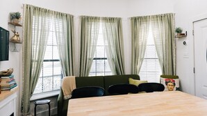 Une pièce chaleureuse avec une table en bois, un canapé vert et une fenêtre ornée de rideaux légers.
