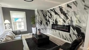 Een moderne woonkamer met een grijze bank, zwarte fauteuils, een zwarte salontafel en een wand met een marmerprint.