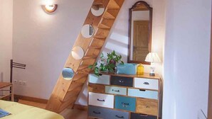 A bedroom with a sloped ceiling, a bed with a yellow bedspread, a dresser with multiple drawers, a mirror, and a small plant on the dresser. - Maison LGBT des Monts Bleus (Moissac-Vallee-Francaise)