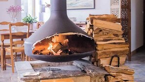 A stone-floored room with a large wood-burning stove, wooden furniture, and a view of the outdoors. - Maison LGBT des Monts Bleus (Moissac-Vallee-Francaise)