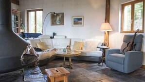 A cozy living room with a stone fireplace, a sofa, a chair, and a guitar. - Maison LGBT des Monts Bleus (Moissac-Vallee-Francaise)