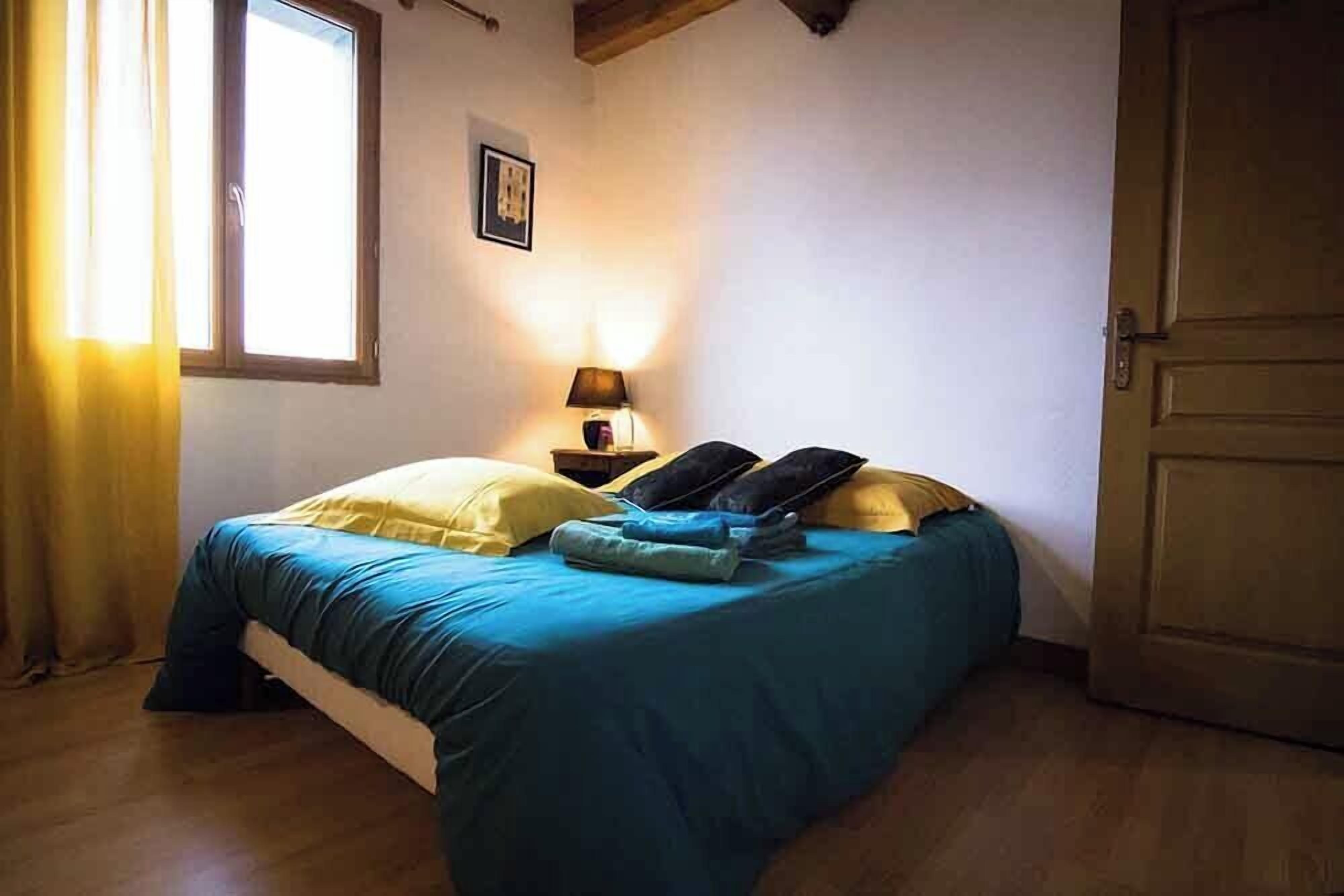A bedroom with a bed, a nightstand, a lamp, a window with curtains, and a door.