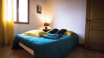 A bedroom with a bed, a nightstand, a lamp, a window with curtains, and a door.