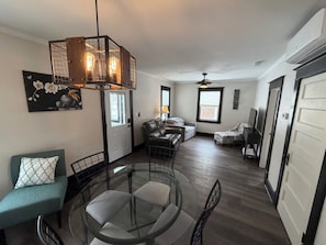 A spacious living room with a glass dining table, leather sofas, and a modern chandelier.