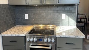 A kitchen with grey cabinets, a granite countertop, a stainless steel stove, and an oven.