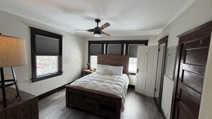 A bedroom with a wooden bed, a ceiling fan, a nightstand, a lamp, and a window with blinds.