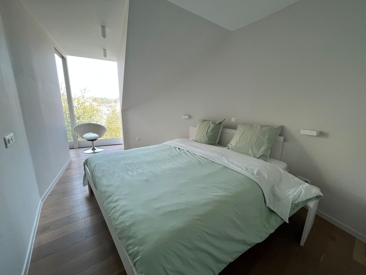 A modern bedroom with a large bed, a chair, and a view of the outdoors.