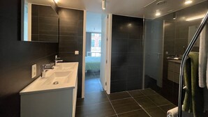 Ein modernes Badezimmer mit dunklen Fliesen, einem weißen Waschbecken und einer Duschkabine aus Glas.
