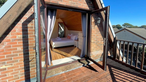 Un dormitorio con suelo de madera, una cama y un ventanal con cortinas.