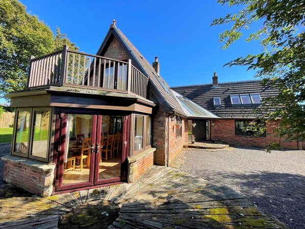 A traditional house with a balcony, a wooden deck, and a gravel driveway. - Beautiful 5BR House near Gretna Green with Garden - Pass the Keys (Kirkpatrick-Fleming)