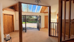 Una habitación amplia con techo alto, vigas de madera, tragaluces y vistas a un jardín.