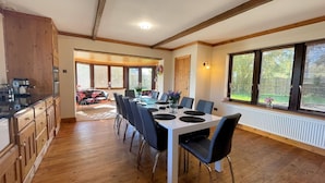 Un comedor con mesa y sillas de madera, una cocina con armarios de madera y ventanas grandes con persianas.