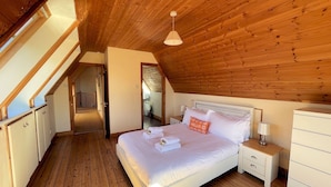 Un dormitorio con techo de madera, una cama con ropa blanca, una mesita de noche y un aparador.