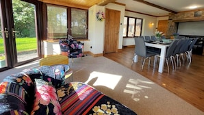 Un espacio habitable amplio con techo de madera, ventanas grandes, una mesa de comedor con sillas y una zona de cocina.
