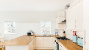 Een moderne keuken met witte kastjes, een houten aanrecht, een ingebouwde oven en een fornuis.
