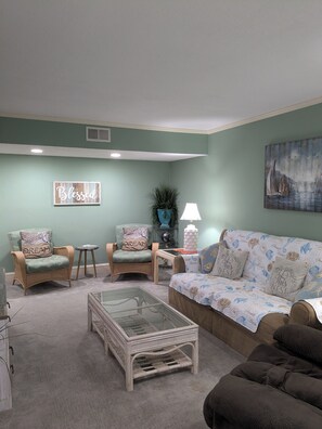 Ein Wohnzimmer mit zwei grünen Sesseln, einem weißen Couchtisch und einem blauen Sofa mit floralem Muster.