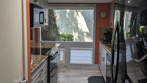 Eine moderne Küche mit Granit-Arbeitsplatten, Edelstahlgeräten und einem großen Fenster mit Blick auf einen Garten.