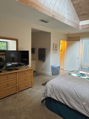 A bedroom with a bed, a dresser, a television, and a door leading to another room. - Cozy 2-bedroom condo with sunroom on a beautiful golf course St. Simons Island.
 (St. Simons Island)