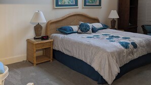 Ein Schlafzimmer mit einem großen Bett, zwei gerahmten Kunstwerken an der Wand, einem Nachttisch mit Lampe, einem Korbstuhl und einem Kleiderschrank.