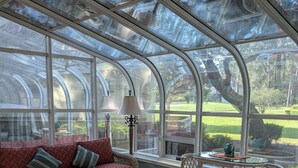 Ein Wintergarten mit einer roten Couch, Korbmöbeln und Blick auf einen Garten.