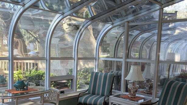 Ein Wintergarten mit Glasveranda, Korbmöbeln und einem gemusterten Teppich.