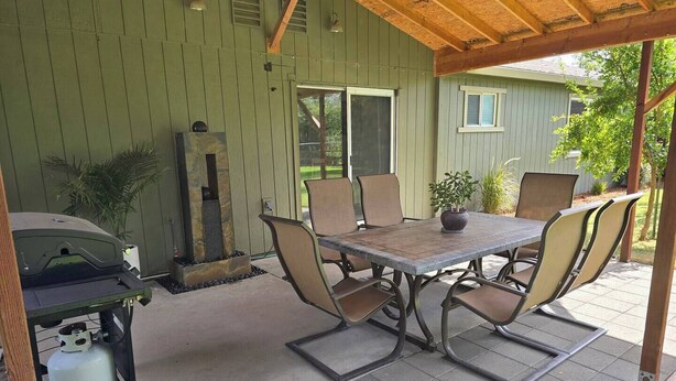 Un patio exterior con una mesa, sillas, una parrilla y una planta en maceta.