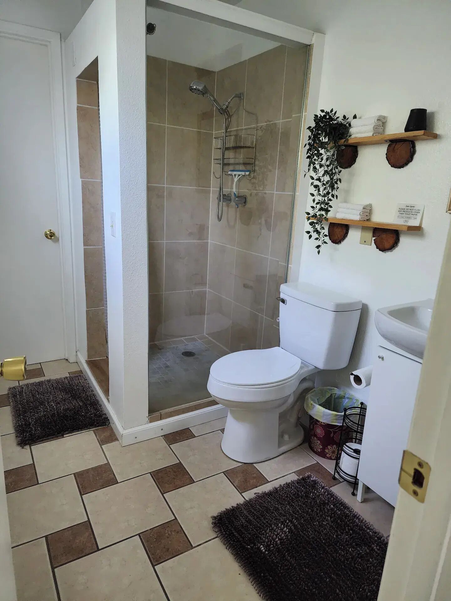 Un baño con ducha, inodoro, lavabo y un estante pequeño con toallas y un cartel.