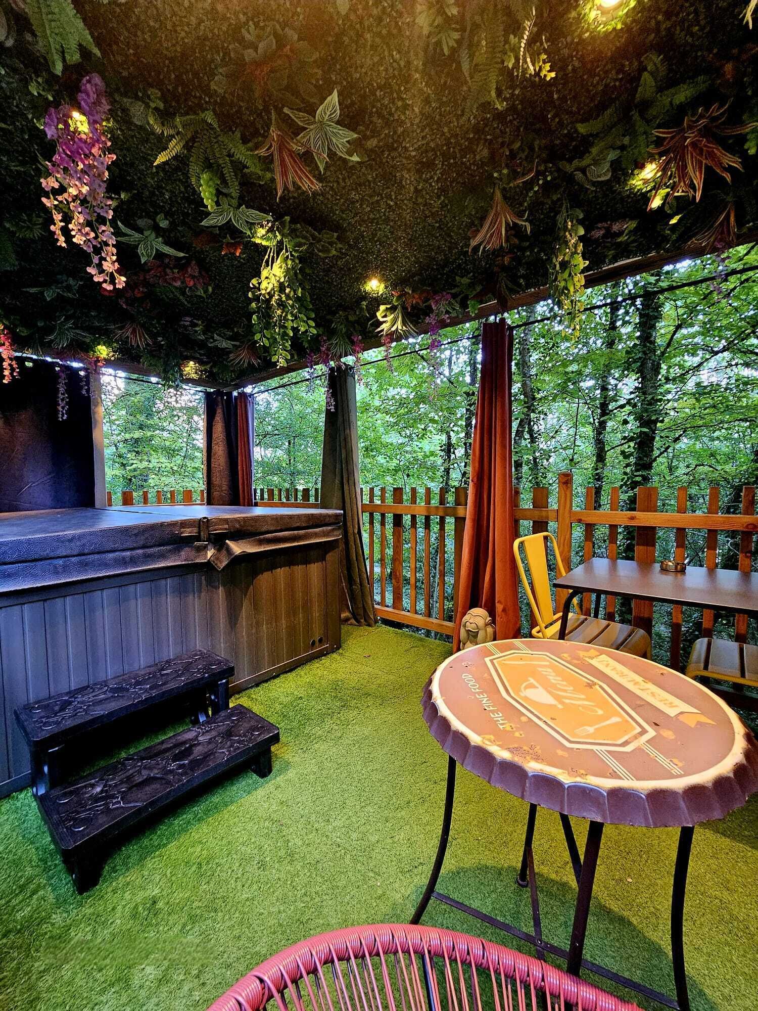 An outdoor seating area with a bar, wooden furniture, and a view of the forest.